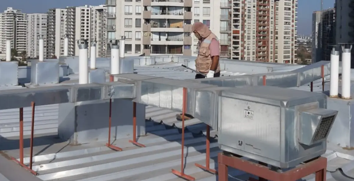 Técnico realizando mantención de cubierta metálica y ductos de climatización en la azotea de un edificio